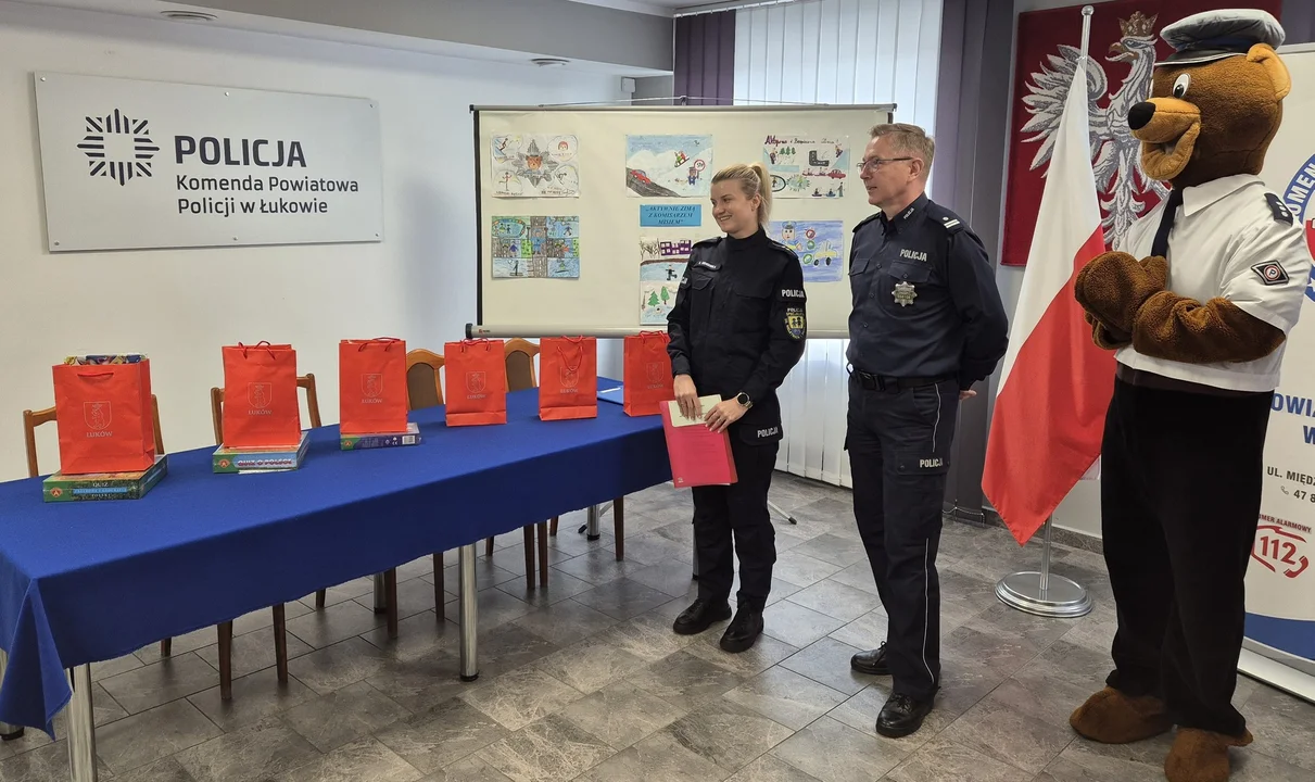 Policjanci i maskotka komisarz Miś, w tle tablica z pracami plastycznymi